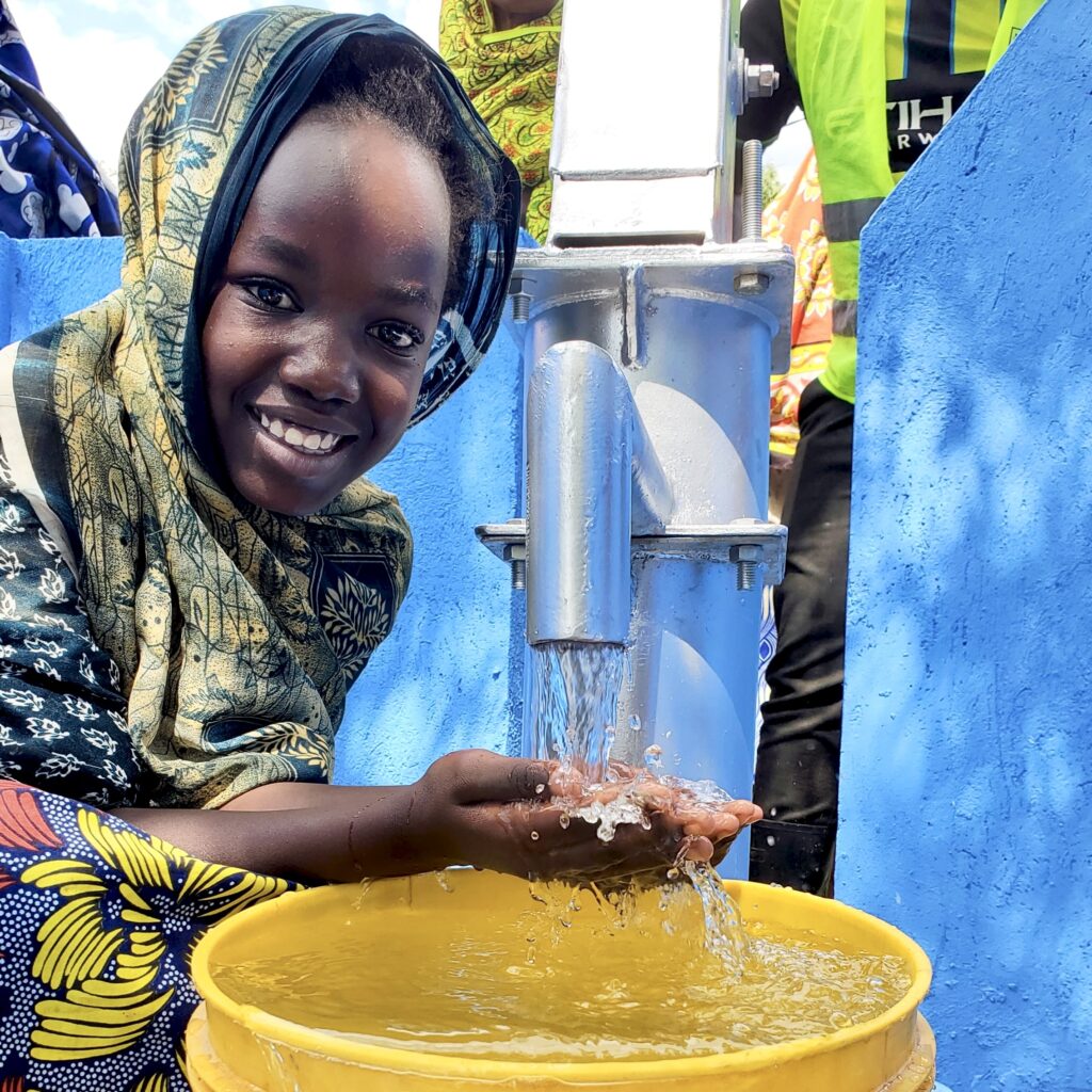 “A smiling girl about to drink clean water flowing from a well”