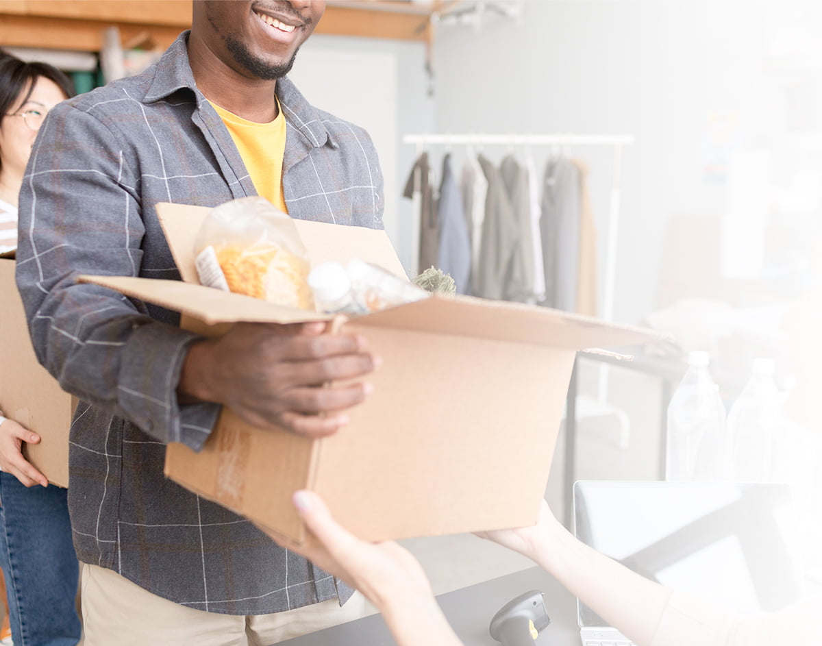 A smiling volunteer handing over a box filled with clothing and material donations.