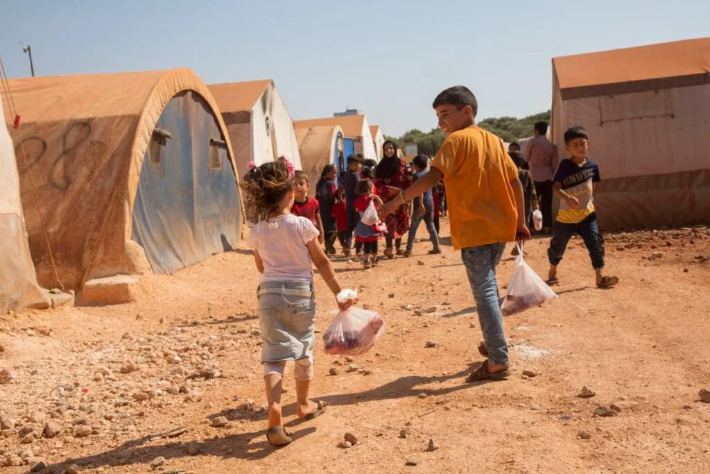Happy children running through a camp holding bags of meat from Kurban donations.