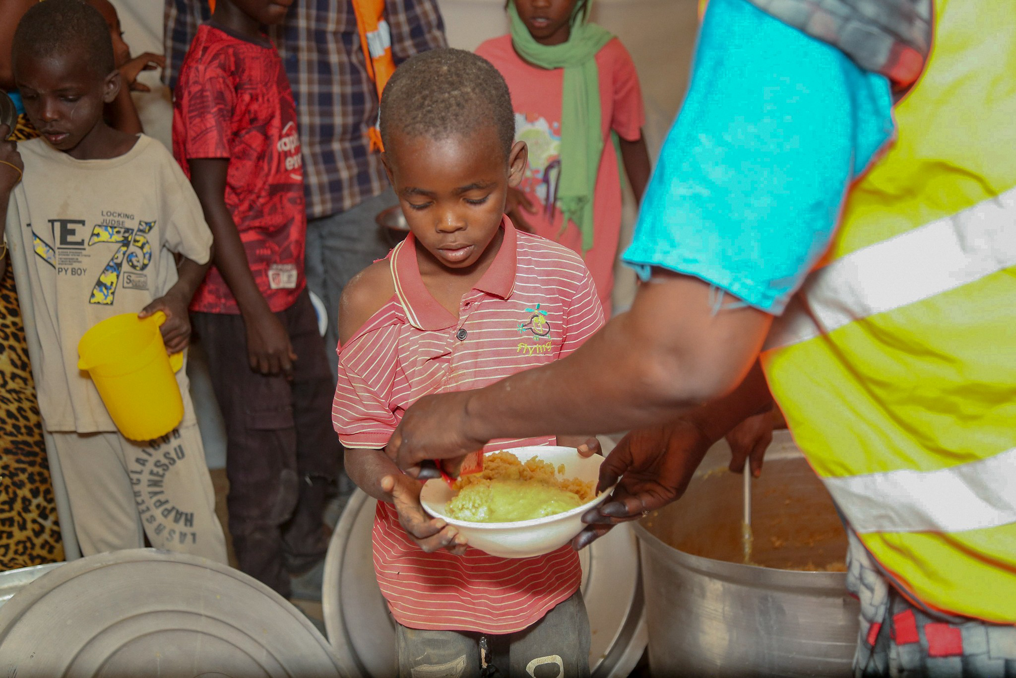 Ein Helfer von Barakah Charity verteilt eine warme Mahlzeit an einen kleinen Jungen im Sudan.