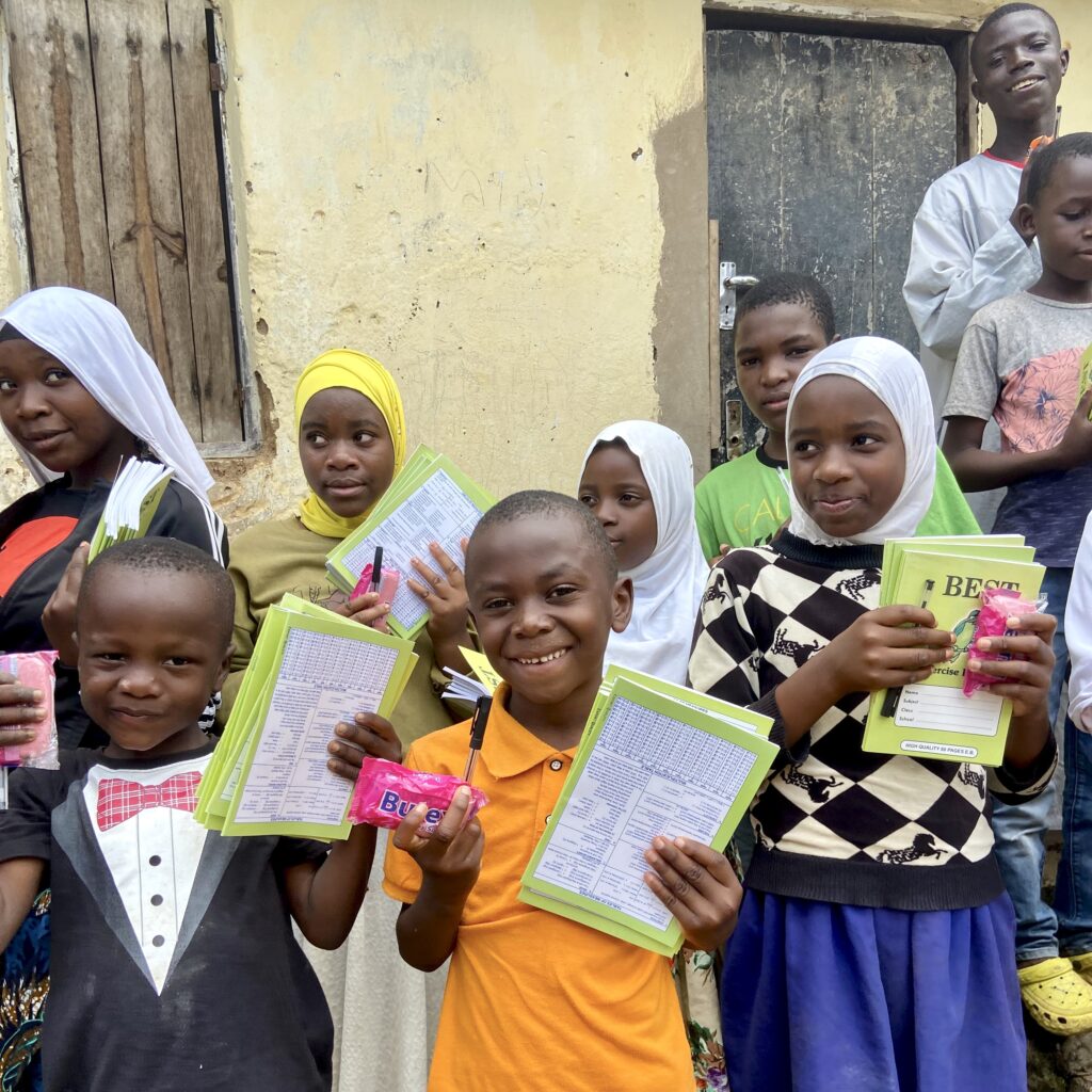 Un groupe d'enfants orphelins sourient en montrant leurs nouveaux cahiers et fournitures scolaires reçus dans un village africain.